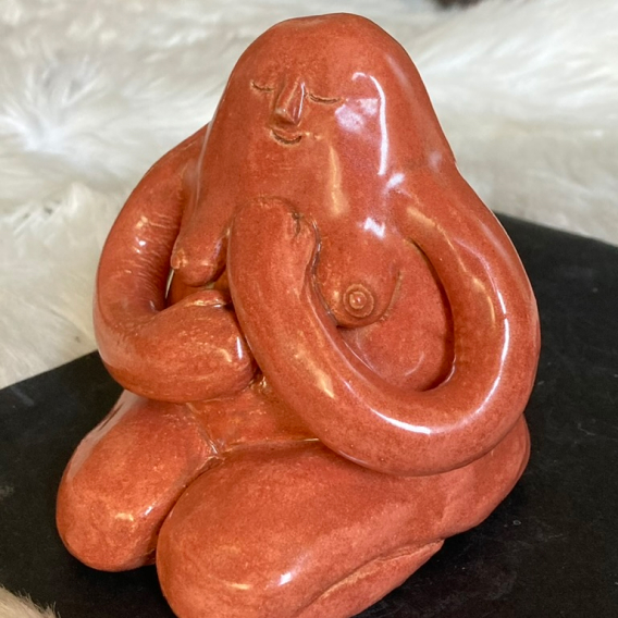 A ceramic figure glazed in burnt sienna hugging itself